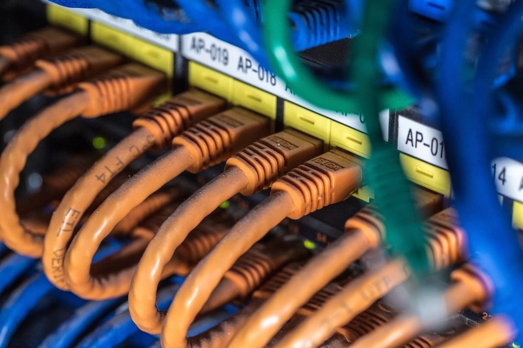 Nahaufnahme eines Patchfelds im Netzwerkschrank mit beschrifteten orangefarbenen und blauen Patchkabeln.