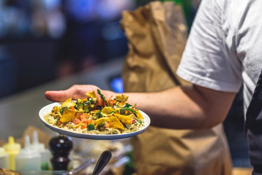 Servicekraft mit Schürze trägt einen frisch angerichteten Teller durch das Restaurant.