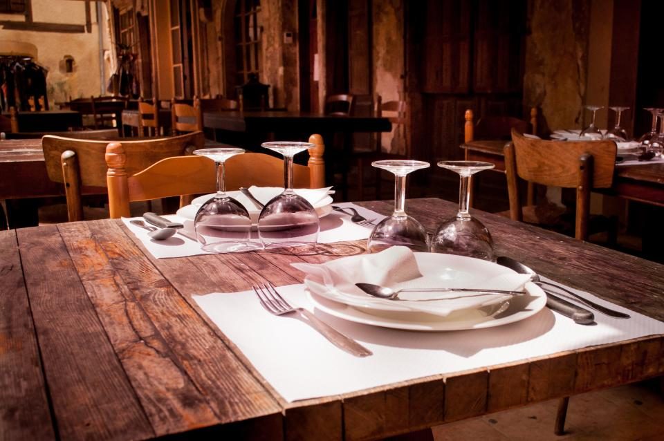 Eingedeckter Holztisch mit Tellern, Besteck und Weingläsern in einem rustikalen Restaurant.